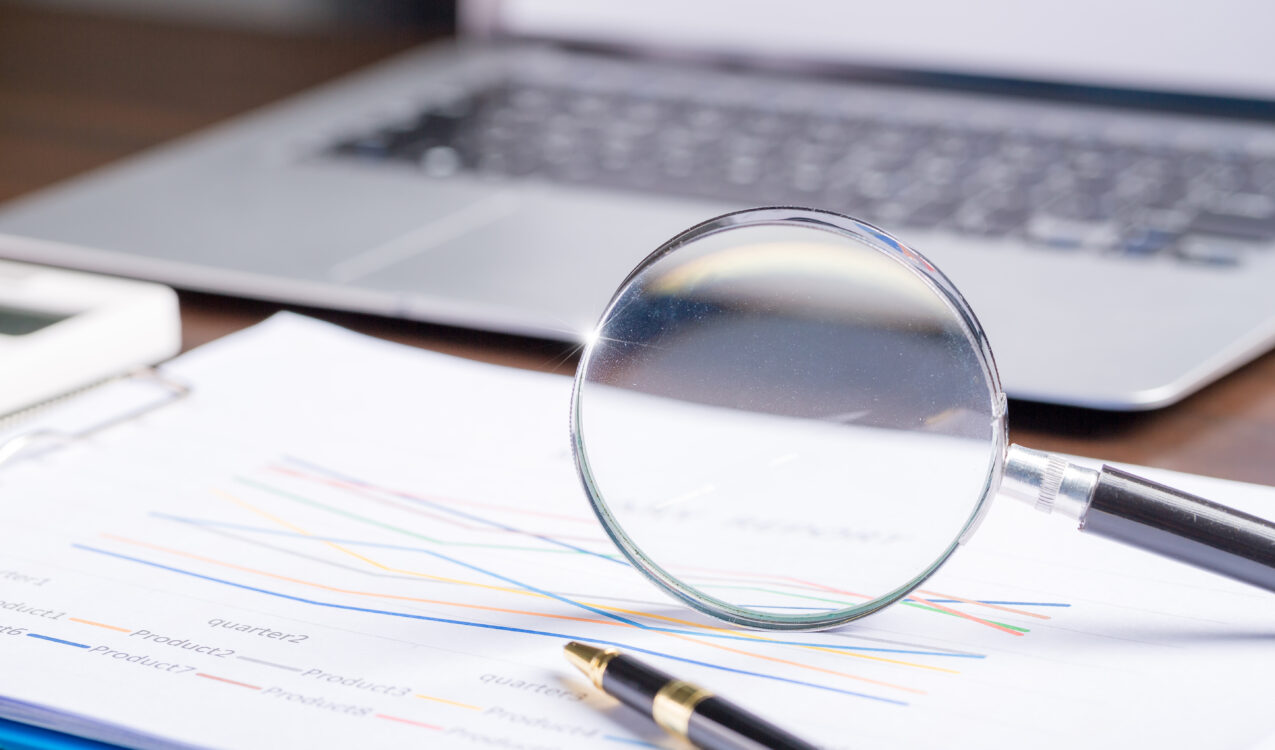 A magnifying glass placed over financial documents and reports, symbolizing the importance of verifying licensed money lenders in Singapore and reviewing loan details carefully with guidance from Khalon & Gill.