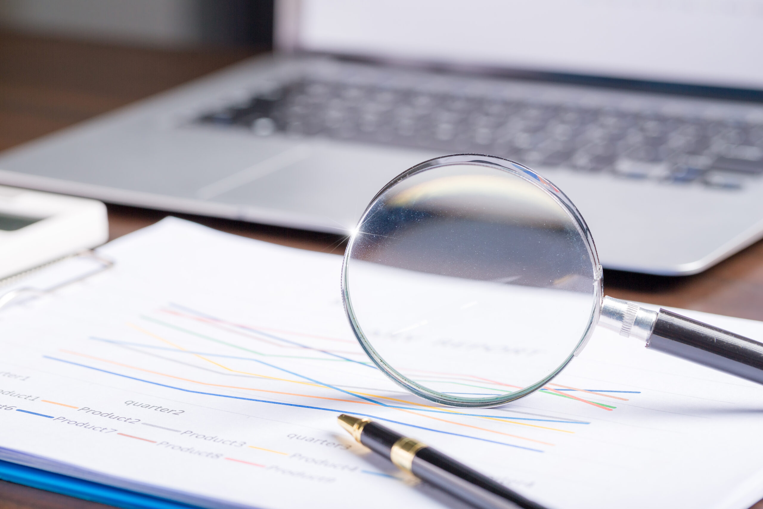 A magnifying glass placed over financial documents and reports, symbolizing the importance of verifying licensed money lenders in Singapore and reviewing loan details carefully with guidance from Khalon & Gill.