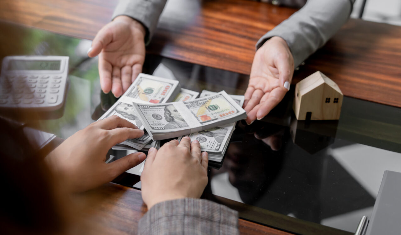 Person reviewing a transparent money lending transaction, with stacks of cash exchanged across a desk, a calculator nearby, and a miniature house model symbolising clear loan terms and financial transparency in Singapore.