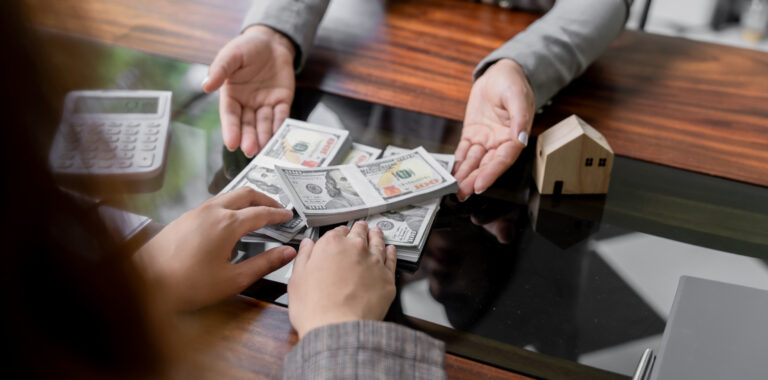 Person reviewing a transparent money lending transaction, with stacks of cash exchanged across a desk, a calculator nearby, and a miniature house model symbolising clear loan terms and financial transparency in Singapore.